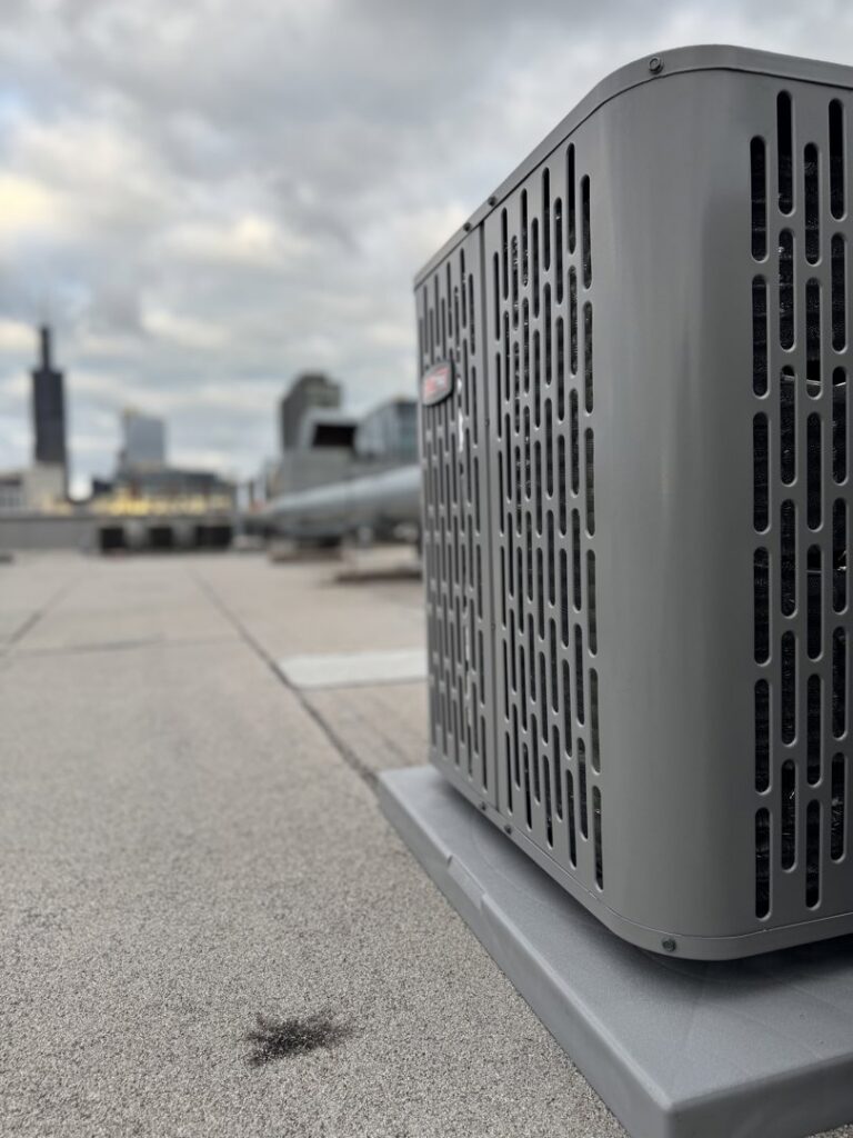 An outdoor air conditioning unit on a rooftop with the Chicago skyline in the background, serviced by Hvac Buddies in Chicago, IL