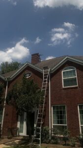 A technician from 832 Home Service on a ladder, performing chimney cleaning and inspection on a rooftop in Houston, TX.
