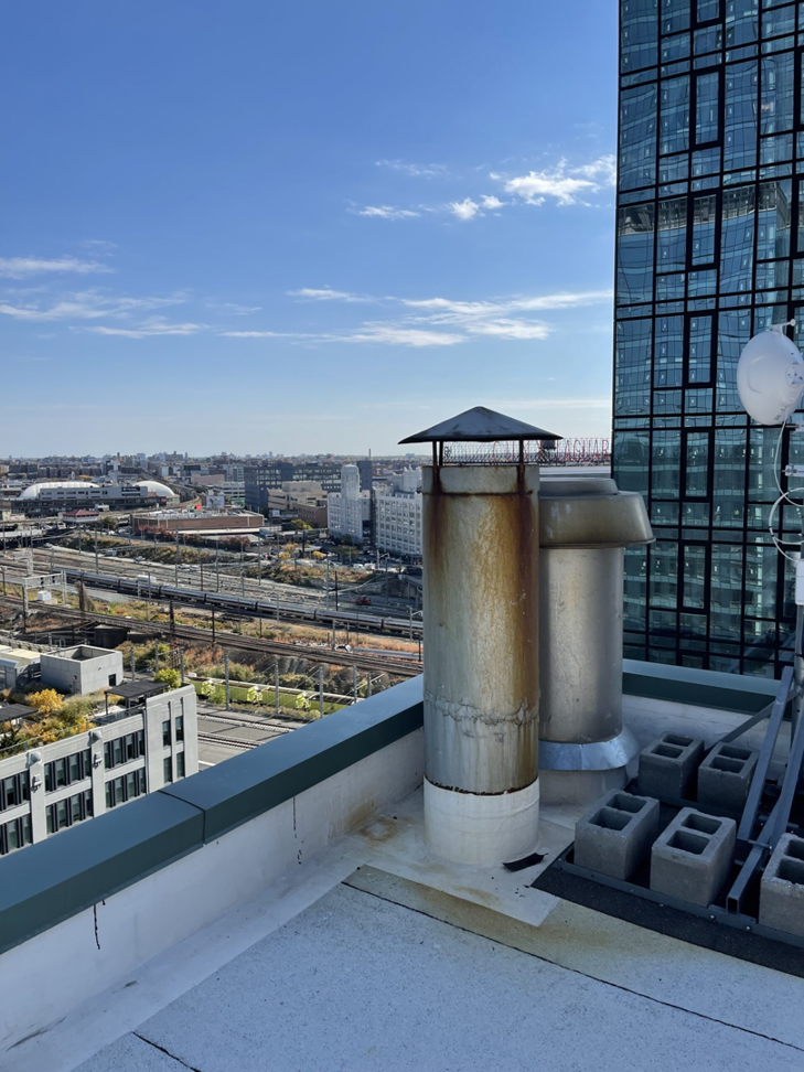Multiple chimneys on a Brooklyn rooftop with a city view, serviced by Chimney Sweep Service LLC.