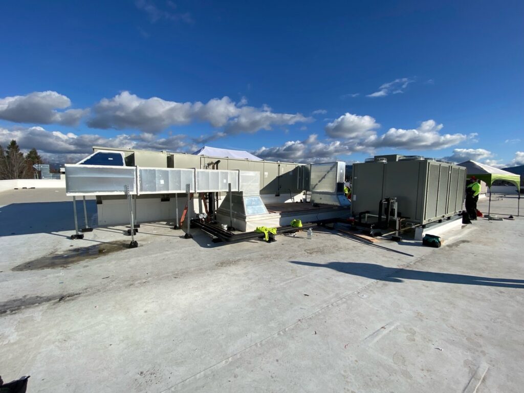 Workers installing large commercial HVAC units and ductwork on a rooftop, performed by ACI Northwest Heating, Cooling & Electrical in Dalton Gardens, ID.