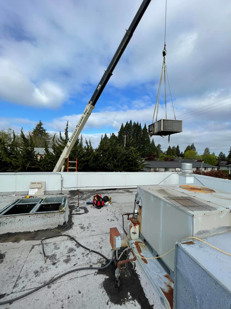 A crane lifting a new HVAC unit onto a commercial rooftop during an installation by Excellence Heating & Cooling, LLC. in Beaverton, OR.