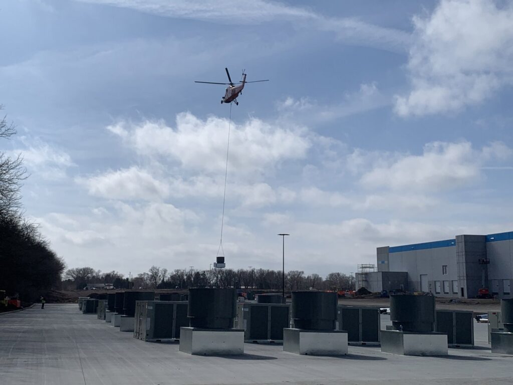 A helicopter lifting a large rooftop HVAC unit during installation by CM3, Inc. in Wichita, KS.
