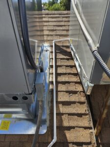 A close-up view of a rooftop HVAC unit with piping and electrical conduit on a shingle roof by Colton Air Conditioning - Las Vegas in Las Vegas, NV.
