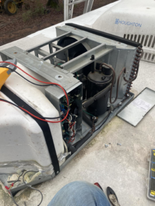 A technician repairing an open rooftop HVAC unit with exposed components for Fox Heating and Air service in Hueytown, AL.