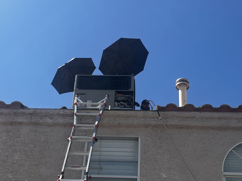 A rooftop HVAC unit being serviced by Blue Collar HVAC in Las Vegas, NV, with umbrellas for shade.