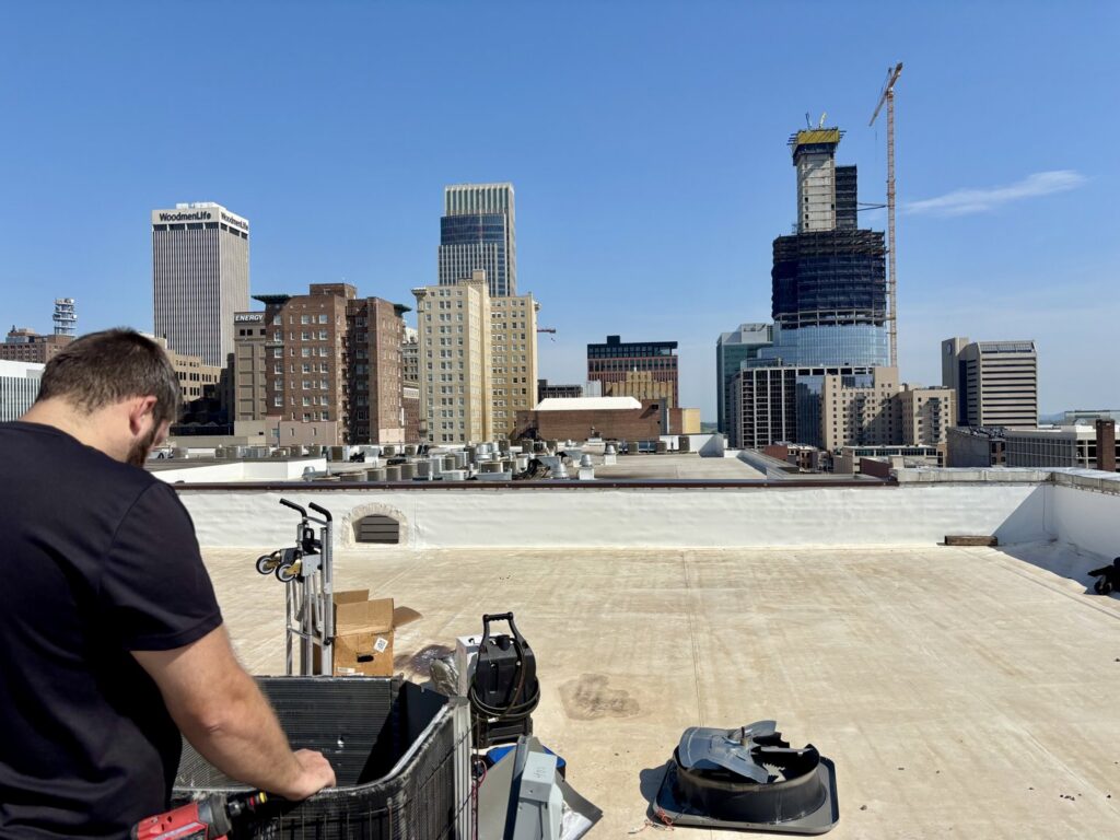 An HVAC technician servicing a rooftop unit with the Omaha skyline in the background for Polar Air Heating and Cooling in Omaha, NE