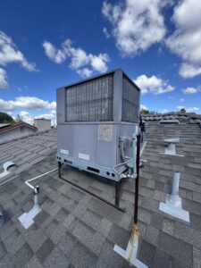 An outdoor rooftop HVAC unit on a shingle roof under a blue sky by Just Chillin' Heating & Air Conditioning, Inc. in Fresno, CA.