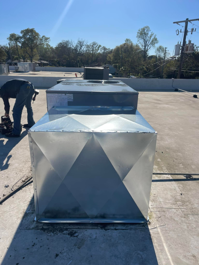 A commercial rooftop HVAC unit with a technician working in the background by Wicked Cool HVAC in Charleston, SC.