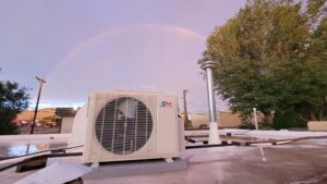 A rooftop mini-split condenser unit installed by Pacheco Air Conditioning and Heating LLC in Albuquerque, NM, with a rainbow.
