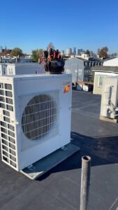 A Mitsubishi mini-split outdoor unit on a rooftop with the Boston skyline in the background, installed by EML Mechanical in Boston, MA.