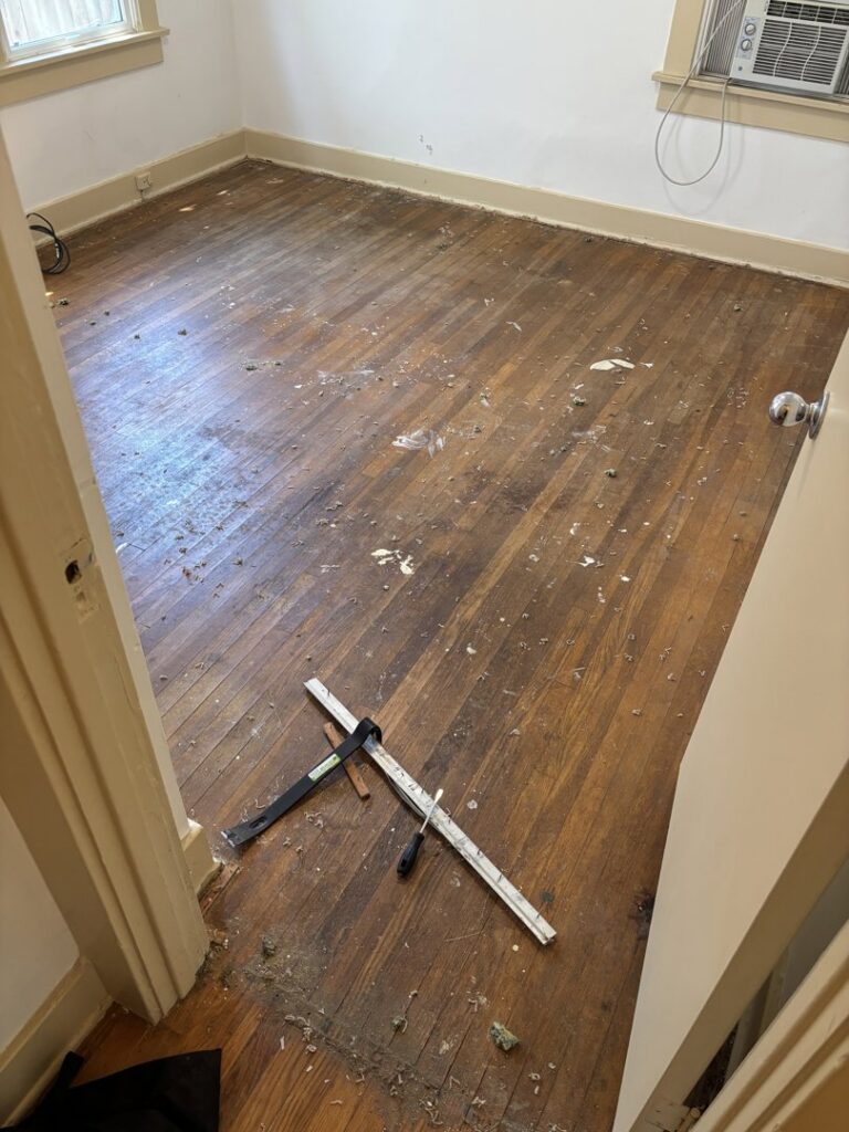 A room showing debris and staples on a hardwood floor after carpet removal by Footprints Floors LA / San Fernando Valley in Studio City, CA.