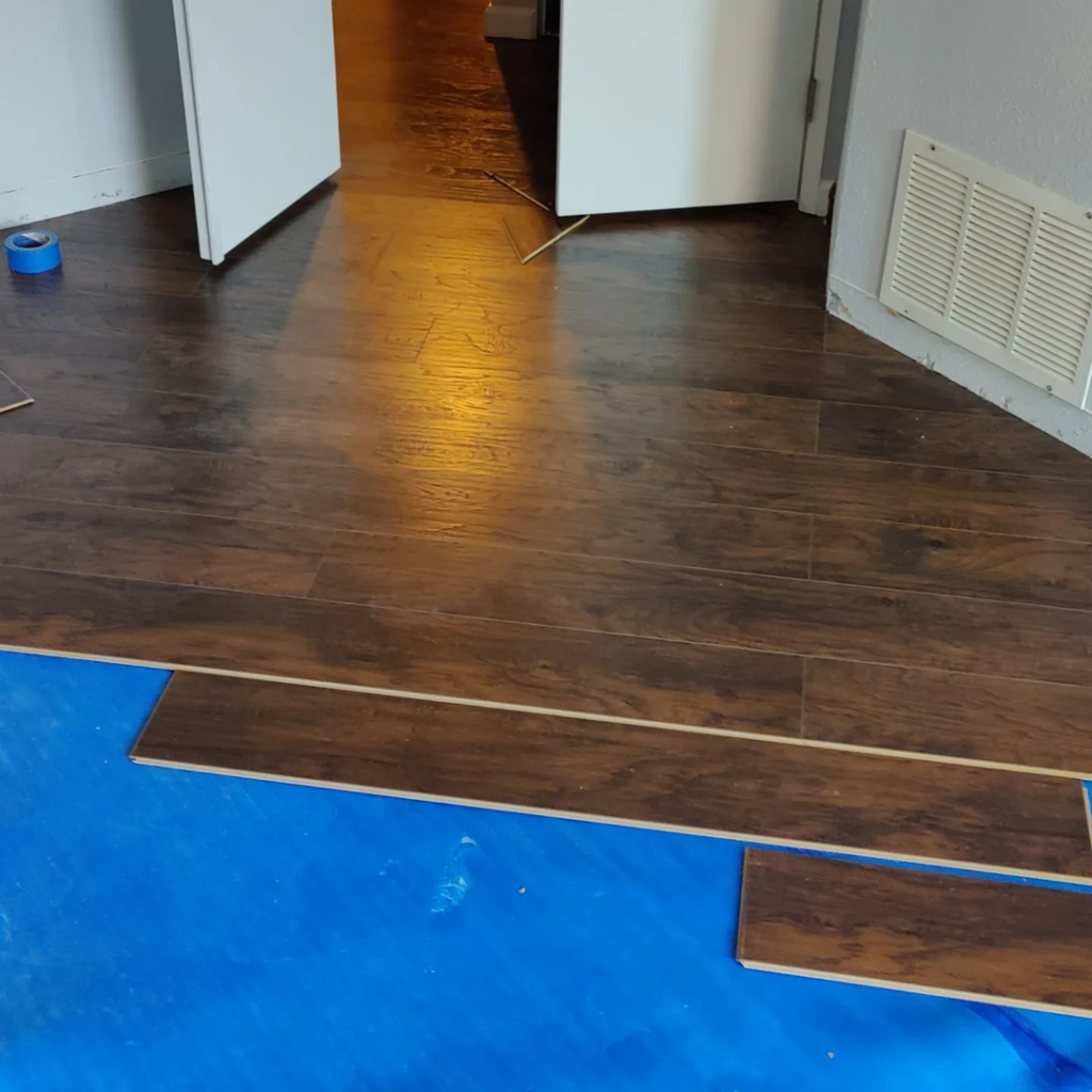 A room with new laminate wood-look flooring partially installed over blue underlayment by Steam Vs. Soil Carpet Cleaning in San Diego, CA