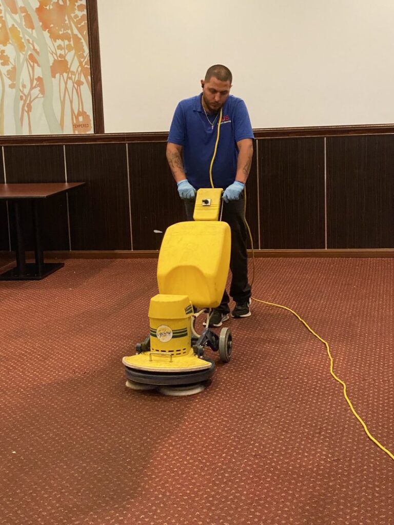 A technician operating a rotary carpet cleaning machine on a red carpet for AJS Carpet Cleaning, Inc. in Orem, UT.