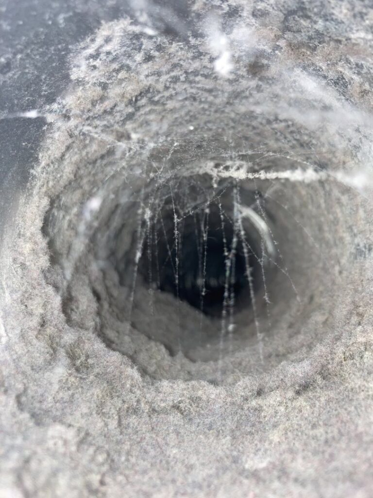 A round air duct opening heavily clogged with lint and cobwebs, showing the need for cleaning by Star Quality Air Duct Cleaning in Silver Spring, MD.