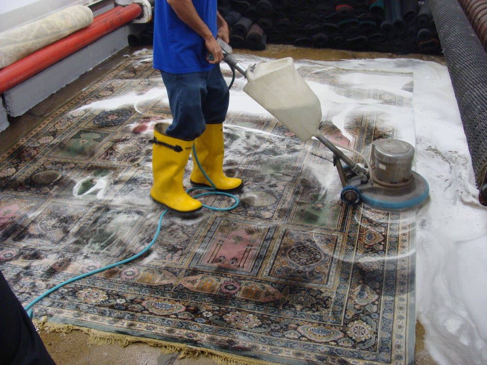 A close-up view of a rug's backing showing a stain, laid over another patterned carpet at Dave's Magikist, Inc. in Milwaukee, WI.