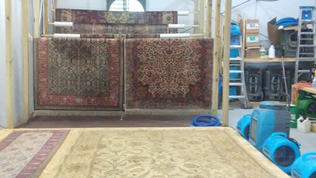 Area rugs hanging on drying racks with air movers in a rug cleaning facility by Tex A Clean Carpet Care in League City, TX.