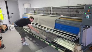 A worker operating a large rug cleaning machine, feeding in a rolled area rug at Personal Touch Carpet Cleaning in Chicago, IL.