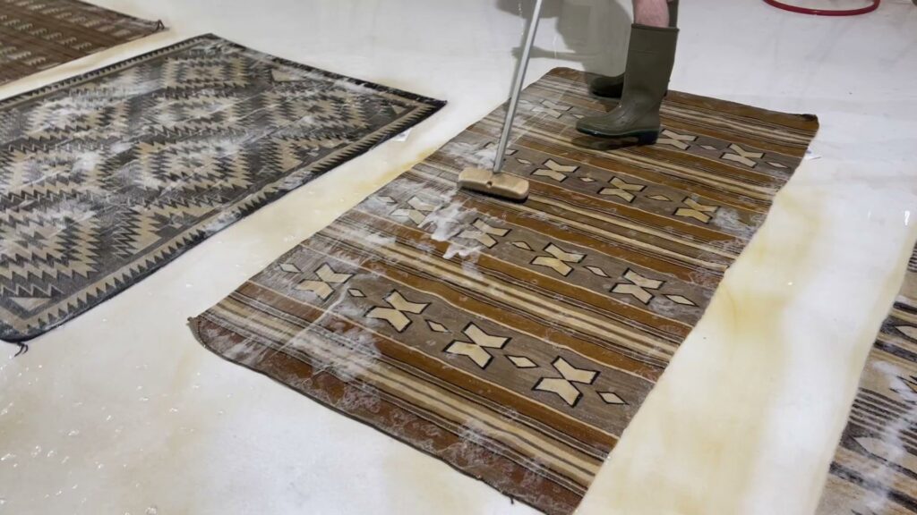 A professional cleaning a rug with a scrub brush and water at Renaissance Rug Cleaning Inc. in Portland, OR.