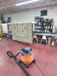 A rug hanging in a workshop with a shop vacuum, indicating rug cleaning services by Muscle Cleaning Services in Dallas, TX.