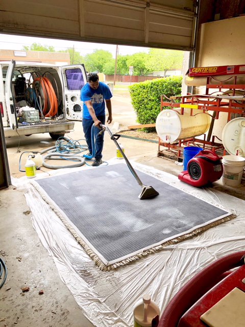 A TLC Carpet Cleaning, Inc. technician cleaning a large area rug in a workshop with a cleaning van in Lewisville, TX.