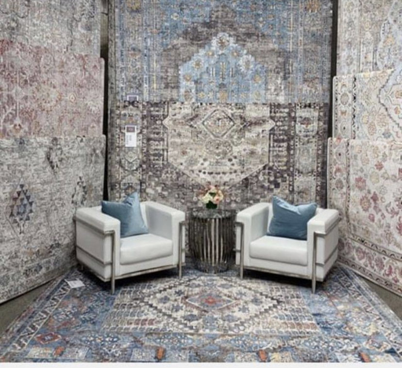 A room showcasing multiple large area rugs on the floor and walls, with two chairs, at Accents Galleria in Kansas City, MO
