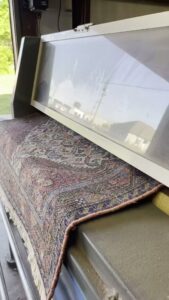 A patterned rug being fed into a professional cleaning machine at Advanced Cleaning Systems in Atlanta, GA.