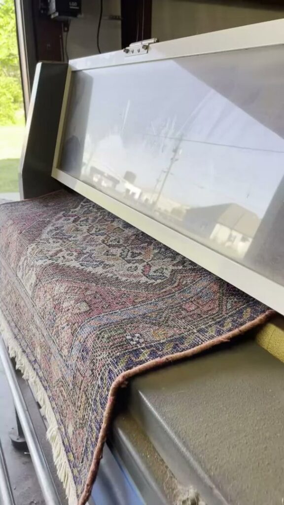 A patterned area rug being fed into a specialized cleaning machine at Advanced Cleaning Systems in Atlanta, GA.