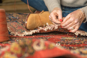 A close-up of hands meticulously repairing the fringe of an oriental rug at Khazai Rugs in Lexington, KY.