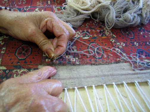 Skilled hands re-weaving or repairing the fringe of a traditional rug at Heriz Rugs, Art, & Interior Design Services in Santa Fe, NM.