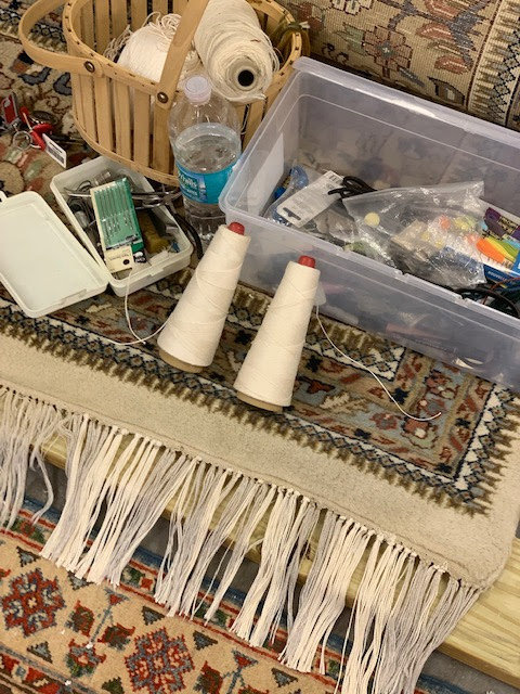 Close-up of rug fringe with spools of thread and repair tools, showing work at Mussallem Area Rug Specialist in Jacksonville, FL.