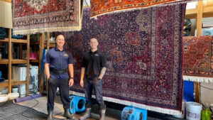 Two Rug Renew staff members standing proudly in front of several large, freshly cleaned rugs hanging to dry in Spring Valley, CA.