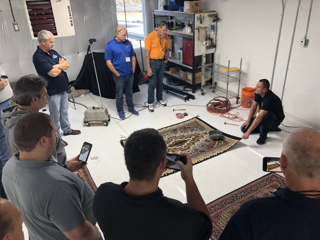 A professional demonstrating rug repair techniques to a group at the Association of Rug Care Specialists in Salem, OR