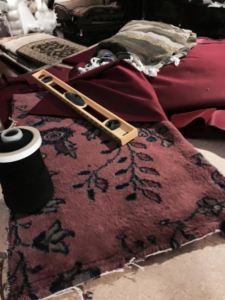 Rug repair materials including a patterned rug piece, thread, and a wooden tool at Tousi Rugs in Los Angeles, CA.