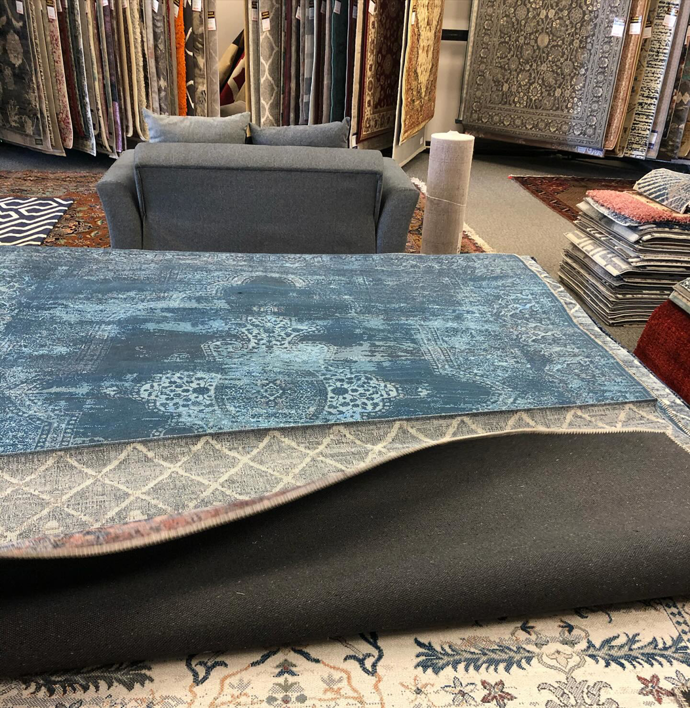 A rug showroom displaying various carpet samples, with one being unfurled, at Adiva Rugs in Chicago, IL.