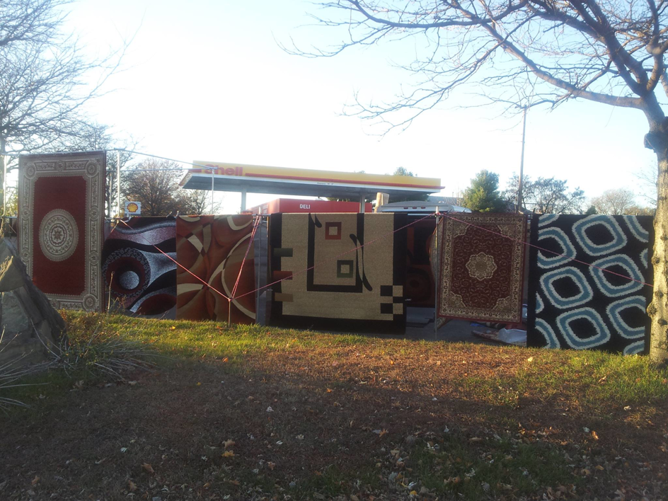 Various patterned rugs displayed outdoors for sale by Sunshine Rugs and Art in Londonderry, NH.