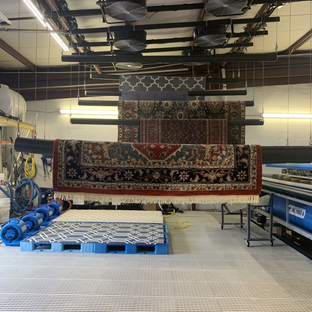 Several rugs hanging on a specialized drying rack after professional cleaning by Winston Salem Carpet Cleaning by Hernandez in Greensboro, NC.