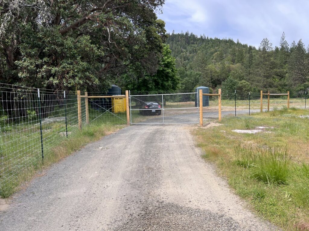 A rural chain-link fence with a gate and wooden posts installed by Prestige Fencing LLC in Medford, OR.