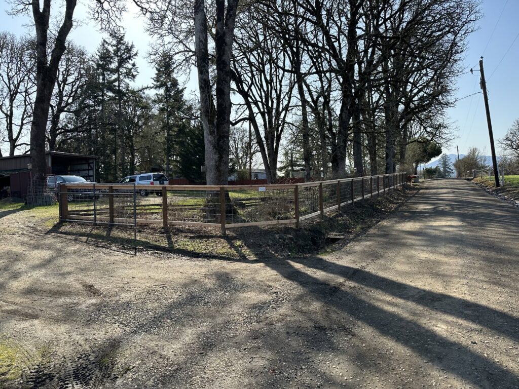 A long wire mesh fence with sturdy wooden posts along a rural road, installed by Faxon Fencing in Corvallis, OR.