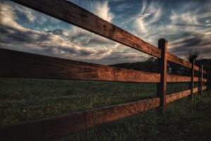 A rustic wooden rail fence in a green field under a dramatic sky by Sumter Fence Company in South Sumter, SC.