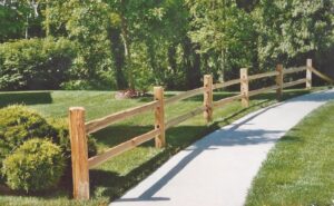 A rustic wooden split-rail fence installed alongside a paved walkway by James Fencing LLC in Columbia, MO.