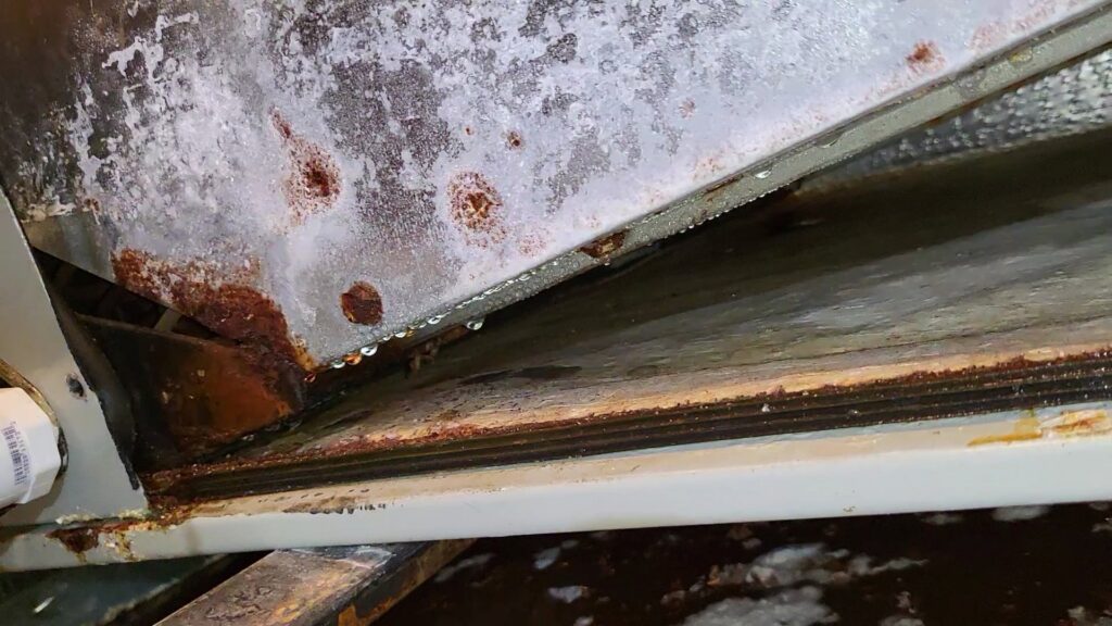 A close-up of a rusty and corroded HVAC drain pan with dripping water, indicating a repair needed from Alien Air Conditioning and Heating in Phoenix, AZ.