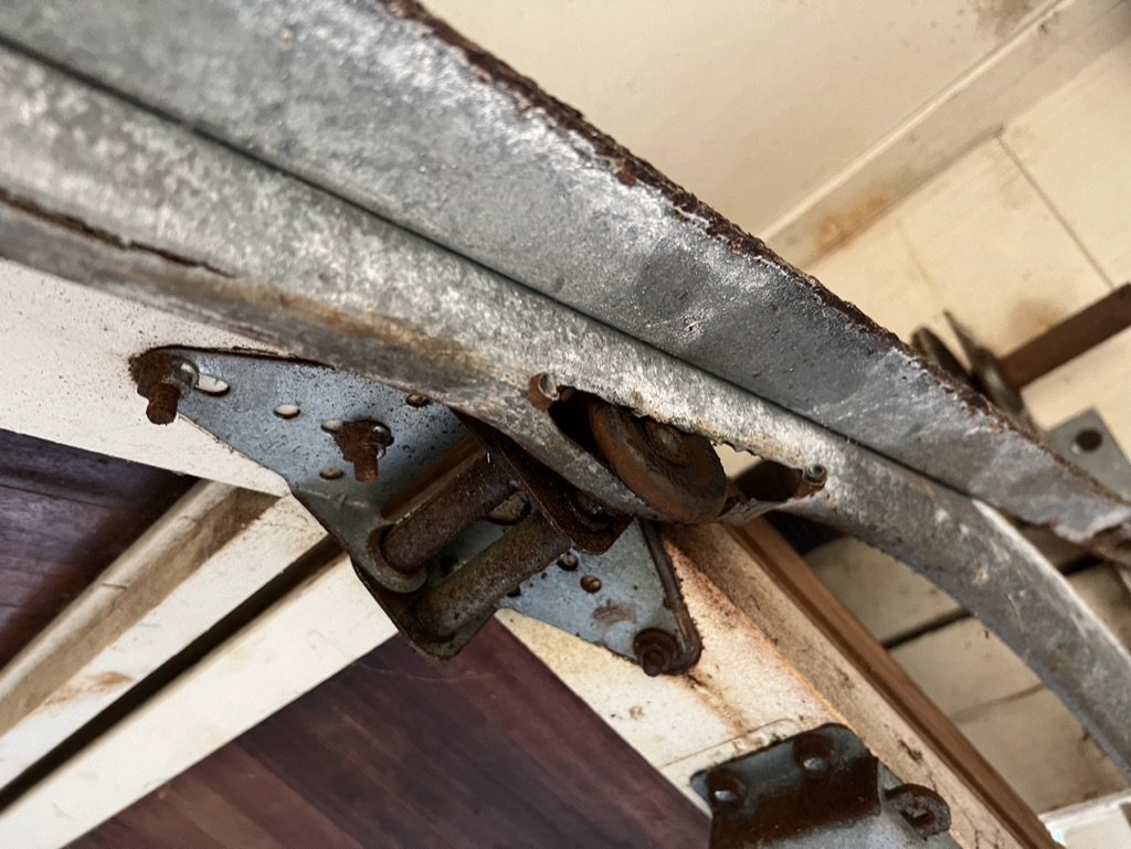 A close-up of a rusty garage door hinge and roller, indicating a need for repair by On Track Garage Doors in Charleston, SC.