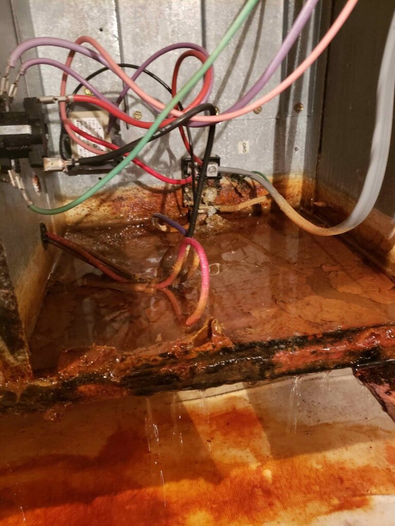 A severely rusty and dirty HVAC drain pan with standing water and exposed wiring, indicating a repair job by Vertex Heating & Cooling in Buckeye, AZ