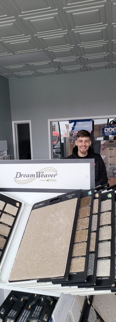 A smiling sales associate standing behind a display of carpet samples at Carpets Direct Naperville, IL.