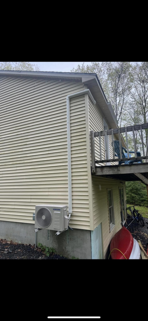 A newly installed Samsung heat pump outdoor unit on the side of a residential building by S&J Heat Pumps in Augusta, ME.