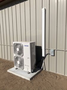An outdoor Samsung mini-split condenser unit installed on a concrete pad next to a building by Crouch's Heating & Cooling LLC in Stillwater, OK.