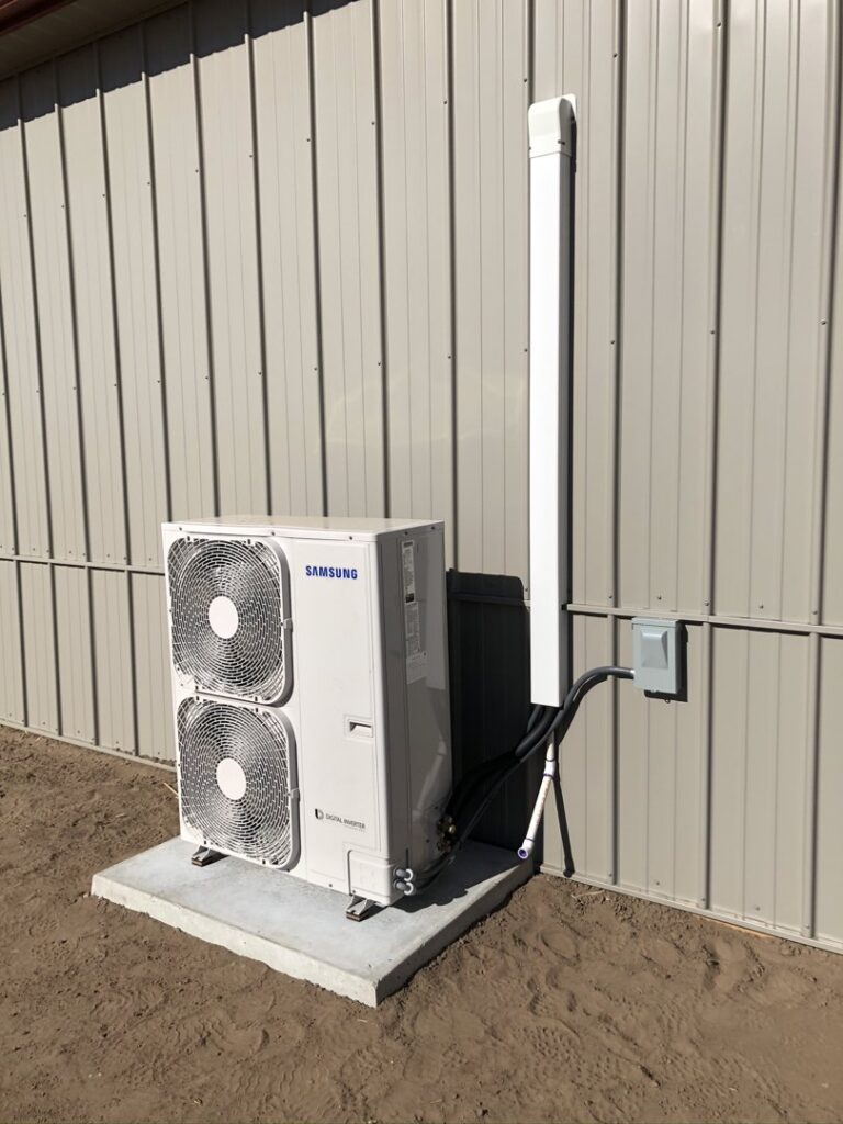 An outdoor Samsung mini-split condenser unit installed on a concrete pad next to a building by Crouch's Heating & Cooling LLC in Stillwater, OK.