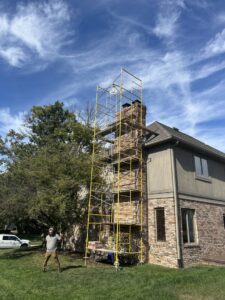 Scaffolding erected around a tall brick chimney on a house, indicating chimney sweep or repair work by Indy Ignited in Indianapolis, IN.