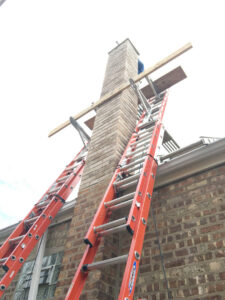 Scaffolding and ladders set up against a brick chimney for repair or construction work by Chimney Usa Inc in Chicago, IL.