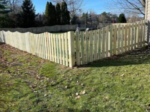 A long wooden privacy fence with a decorative scalloped top, installed in a residential yard by NBBJ Fence LLC in Bluffton, IN.